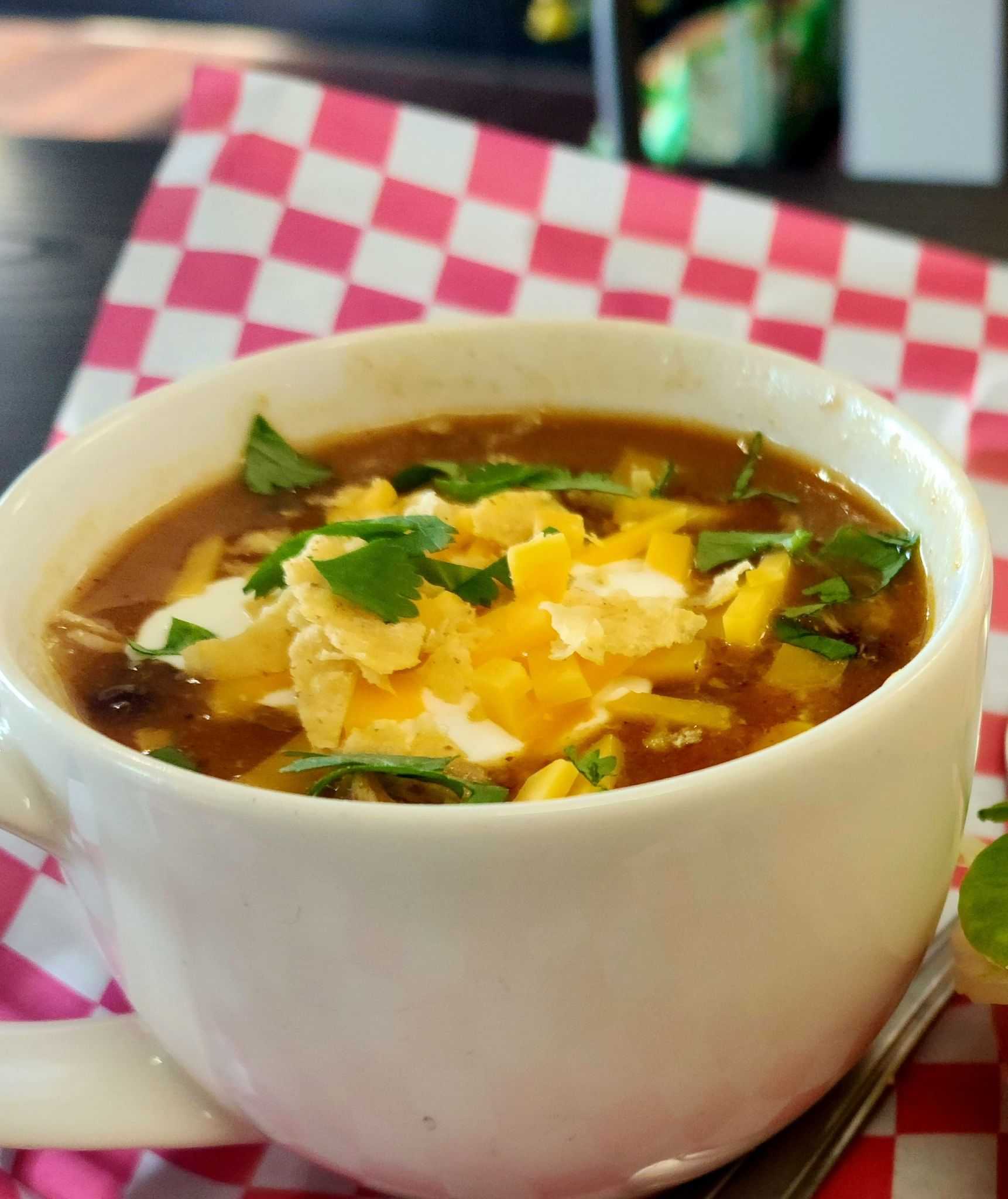 Bowl of chili topped with cheese and herbs on a red checkered tablecloth.